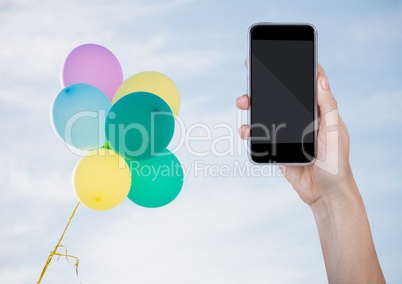 Hand with phone against sunny sky and balloons