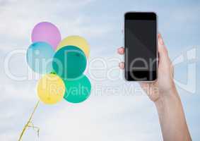 Hand with phone against sunny sky and balloons