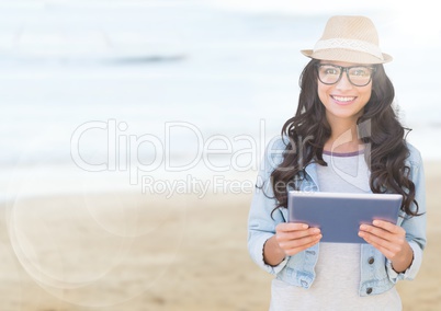 Trendy woman with tablet against blurry beach with flare