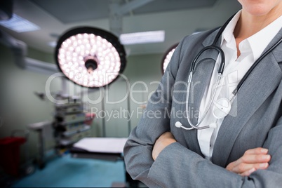 doctor with crossed arms is holding a stethoscope against operating room background