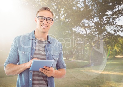 Man with tablet against sunny park with flare