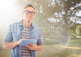 Man with tablet against sunny park with flare