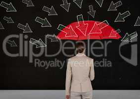 Rear view of businesswoman standing against blackboard holding red umbrella with arrows pointing