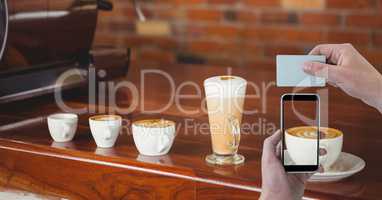 Hand photographing cup of cappuccino with smart phone while holding card in coffee shop