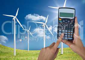 Hands holding calculator on wind farm against sky