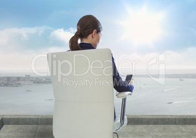 Rear view of businesswoman sitting on chair while looking at mobile phone against sky during sunny d Rear view of businesswoman sitting on chair while looking at mobile phone against sky during sunny d