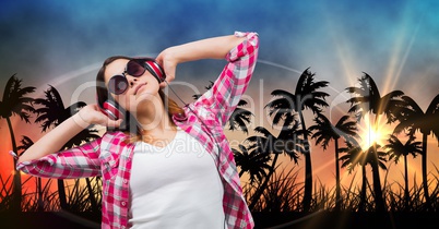 Beautiful woman listening music through headphones while standing against silhouette trees