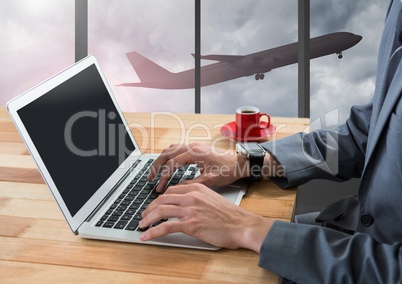 Businessman using laptop in airport with plane at window