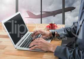 Businessman using laptop in airport with plane at window
