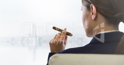 Over shoulder of seated business woman smoking cigar and looking at blurry white skyline