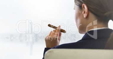 Over shoulder of seated business woman smoking cigar and looking at blurry white skyline