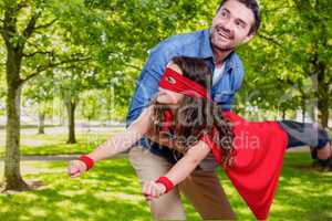 A men carrying a girl disguised into superhero against park background