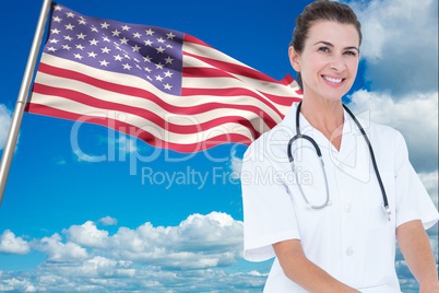 doctor wearing white coat and stethoscope in front of american flag against sky background
