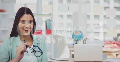 Portrait of businesswoman holding eyeglasses with laptop at office
