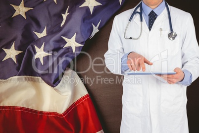 doctor wearing a stethoscope and a white blouse is touching a tablet computer against american flag