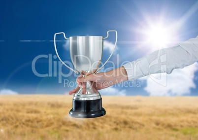 business hand with trophy in a field with blue sky