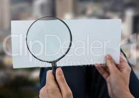 Magnifying glass in hands looking at paper over city