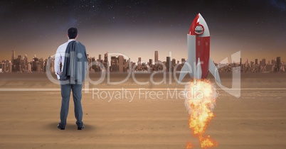 Rear view of businessman standing by rocket launch while looking at city