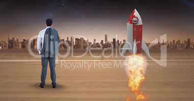 Rear view of businessman standing by rocket launch while looking at city