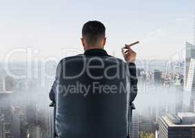 Rear view of businessman sitting on chair and looking at city while smoking cigar