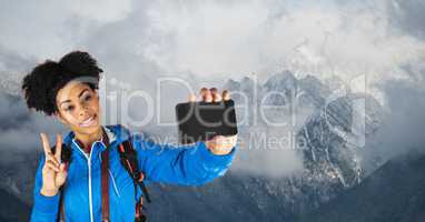 Hipster taking selfie and gesturing peace sign while standing against snowcapped mountains