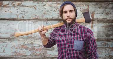 Hipster holding axe while standing against wooden wall
