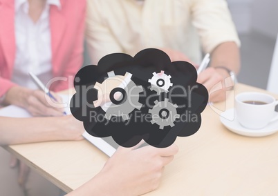 People at table with tablet behind grey cloud and gear graphic