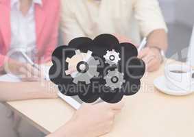 People at table with tablet behind grey cloud and gear graphic