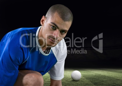 soccer player tying the laces in the field with a ball behind him