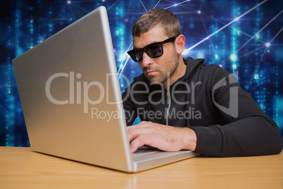 Cyber criminal wearing black glasses is hacking from a laptop on a desk against matrix code rain bac
