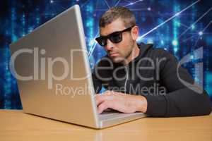 Cyber criminal wearing black glasses is hacking from a laptop on a desk against matrix code rain bac