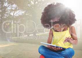 Girl with tablet against blurry park with flare
