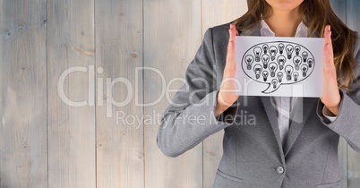 Business woman mid section with card showing speech bubble and lightbulb doodle against wood panel