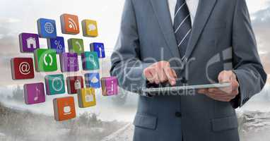 Businessman holding tablet with apps icons outside in landscape
