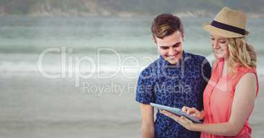 Trendy man and woman with tablet against blurry beach