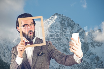 Man taking a selfie with a frame in front of snow-covered mountains
