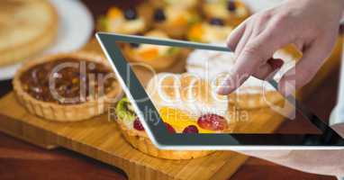 Hand photographing tarts through digital tablet at bakery
