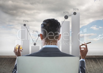 Rear view of businessman sitting on chair with glass of alcohol examining graph while smoking cigar