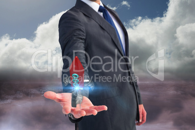 Business man holding a rocket on his hand against sky background