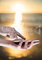 Hands touching phone against blurry sunset beach