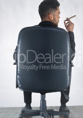 Back of seated business man smoking cigar against white wall with wood floor