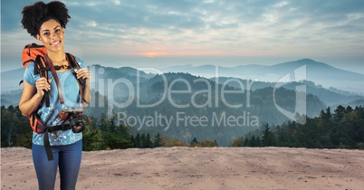 Portrait of smiling hipster carrying backpack with camera standing on road against mountains