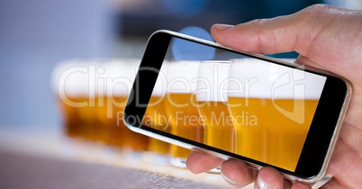 Hand photographing beer glasses through smart phone at bar