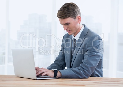 Businessman on laptop against bright windows with city