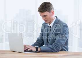 Businessman on laptop against bright windows with city