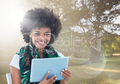 Woman with tablet against sunny park with flare