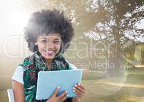 Woman with tablet against sunny park with flare