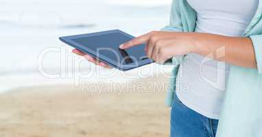 Woman mid section with tablet against blurry beach