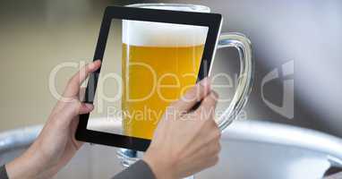 Hands photographing glass of beer through digital tablet at bar