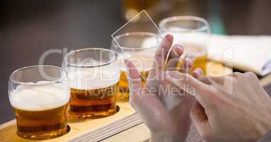 Hands taking picture of beer glasses through transparent device at bar